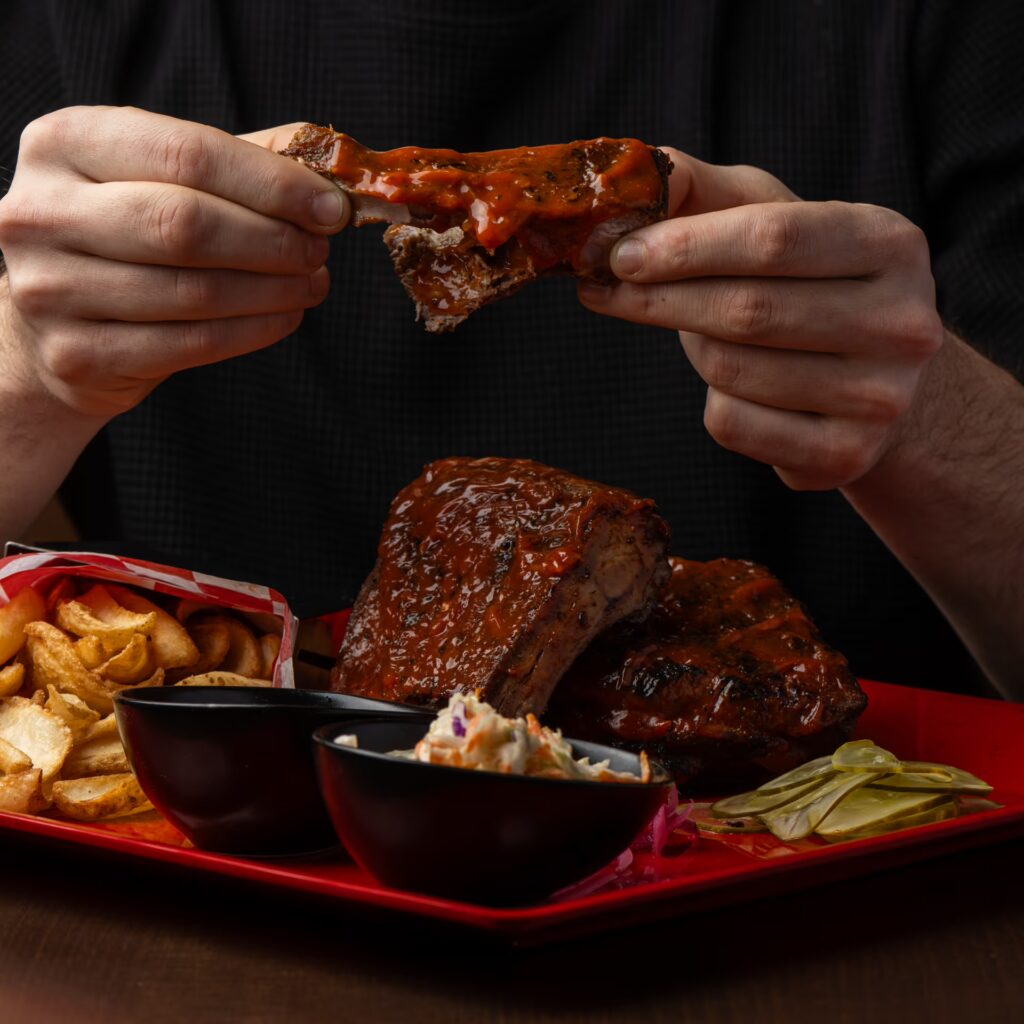 Signature BBQ ribs and fries being enjoyed by a guest at the Planet Hollywood NYC Times Square restaurant.