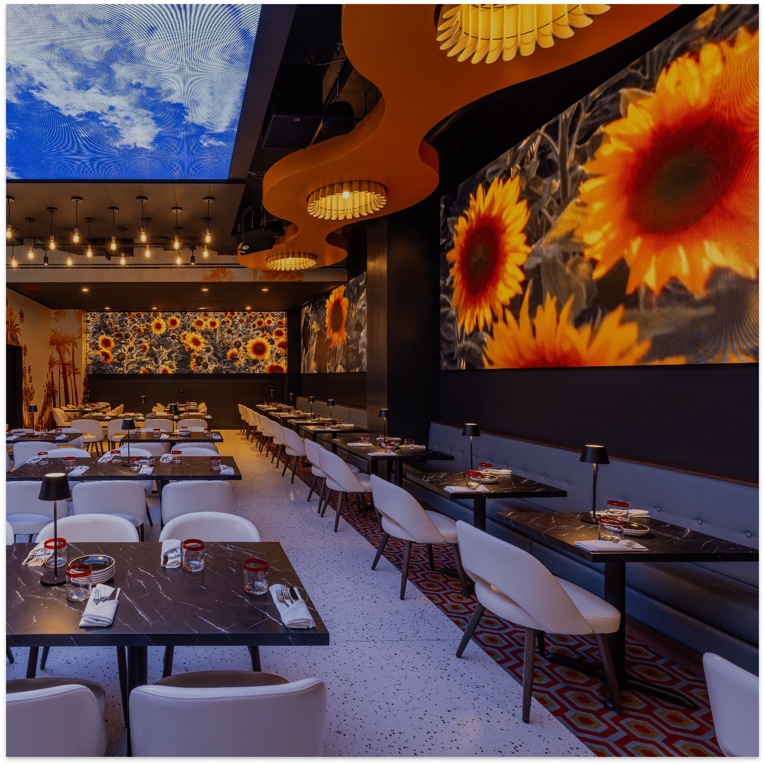 Planet Hollywood NYC dining room with sunflower projections, sculptural orange ceiling lights, white chairs, and black tables.