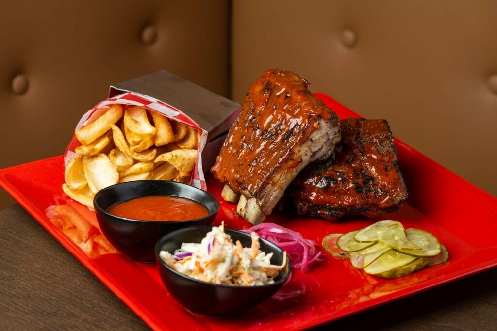 A huge plate of ribs, fries, slaw, pickles, and barbeque sauce