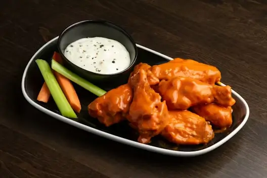 A plate of twice cooked Buffalo wings with celery and ranch