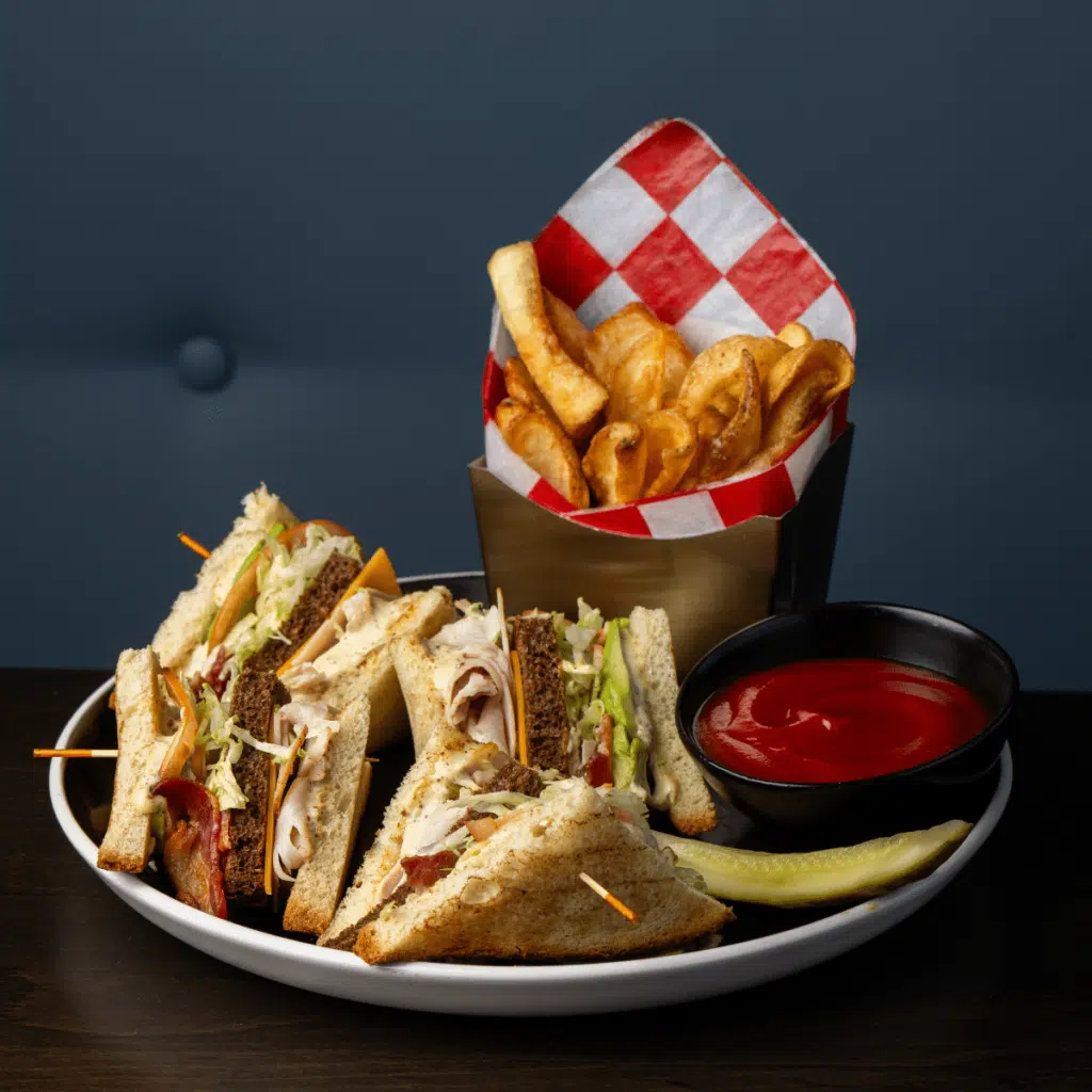 A turkey club, fries, ketchup, and a pickle