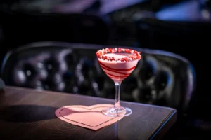 Valentini cocktail with pink and white swirl and red candy rim in a martini glass.